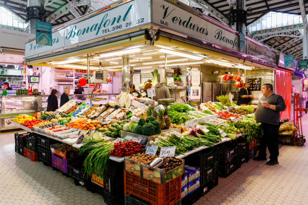Valencia, Spain. Monday,  18th of November 2024. The photo captures a vibrant scene inside the iconic Central Market of Valencia, Spain. Known locally as Mercado Central, this historic market is one of Europe’s oldest functioning food markets and a landmark of modernist architecture. The interior features a stunning combination of historical charm and contemporary functionality, with colorful stalls offering fresh produce, meat, fish, and regional delicacies. Natural light streams through the market's glass windows, highlighting the intricate ironwork and decorative ceramic tiles. This image perfectly encapsulates the dynamic atmosphere of this cultural hub, making it ideal for travel publications, culinary blogs, or architectural features.