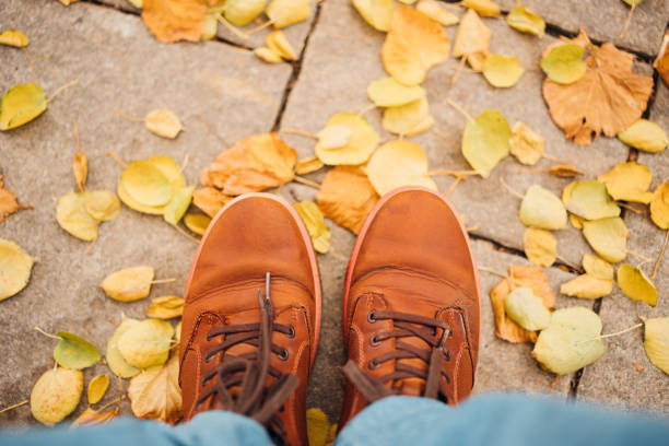 Brown leather men's boots on a path with fallen autumn leaves. walks around the city.