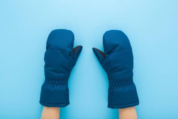 Little child boy hands in dark blue waterproof warm winter mittens on light blue table background. Pastel color. Closeup. Point of view shot. Top down view.