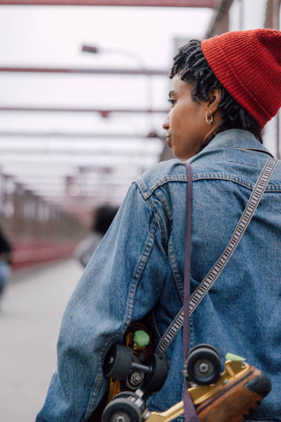 Young woman bringing roller skates on shoulder while walking up Williamsburg Bridge in Brooklyn, New York.