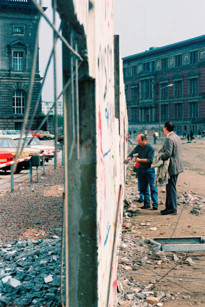 Military soldiers guarding holes in the Berlin Wall in 1990 shortly after its fall. Berlin, Germany - 01 FEB 1990 - View of both East and West of Berlin Wall 1989 - Shortly after the fall of the Wall. Man chisels away at the wall to remove pieces for sale. 1980 1989 stock pictures, royalty-free photos & images