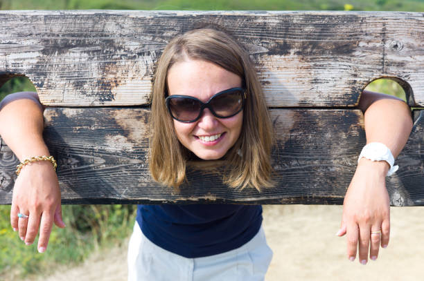 Visiting Brittany France. Fort de la Latte is a stunning ancient building perched on the rocky coast of Brittany, a place to visit. Here a beautiful woman jokingly poses locked up in a pillory. medieval restraints stock pictures, royalty-free photos & images