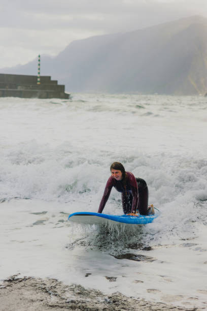 Side view of female in pink wetsuit surfing at majestic Sexial beach, feeling freedom and happiness on Madeira island, Portugal