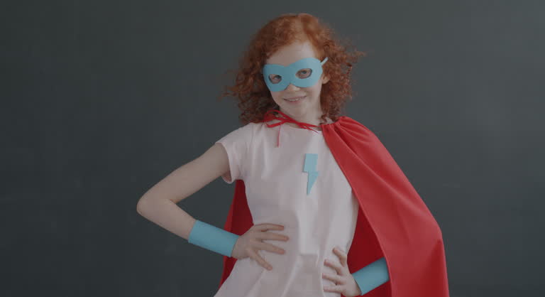 Slow motion portrait of confident girl in superhero costume standing akimbo on grey color background