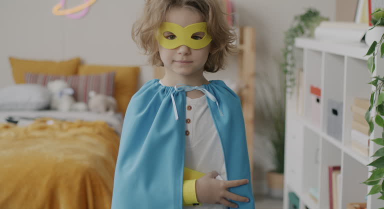 Slow motion portrait of child with blond curly hair dressed-up in masquerade superhero costume standing at home