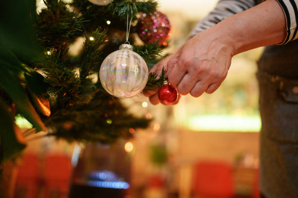 Close up to hands hanging knick knacks on Christmas tree.