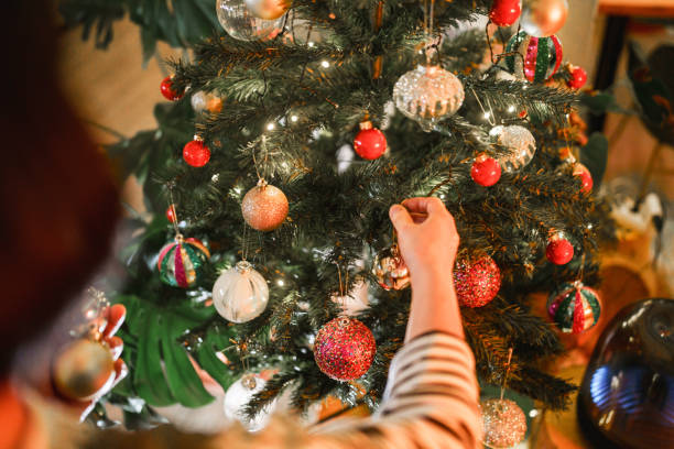 Close up to hands hanging baubles on Christmas tree.