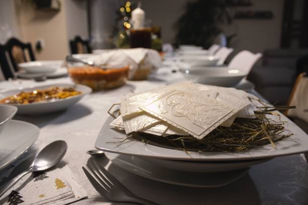 Festive dining table set for Christmas Eve with white plates, hay, and traditional wafers, creating a warm holiday atmosphere.