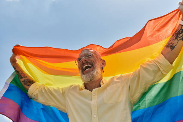 istock Joyful mature man celebrates pride with vibrant rainbow flag under a clear blue sky 2186215015