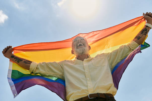 istock Mature man joyfully celebrates pride with rainbow flag under the sunny sky 2186215017