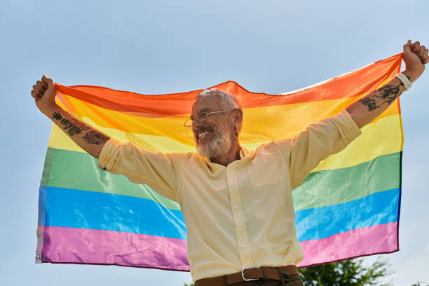 istock Mature man joyfully celebrating pride while holding a vibrant rainbow flag under a clear sky 2186215059