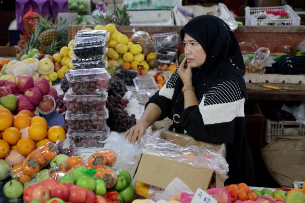 Focus on Muslim woman is using smartphone talking while selling fresh fruits at Asian morning market