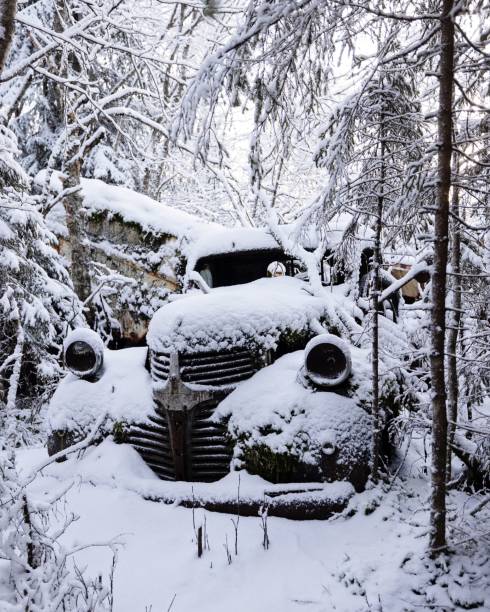 A vintage car covered in snow, abandoned in a dark, snowy forest