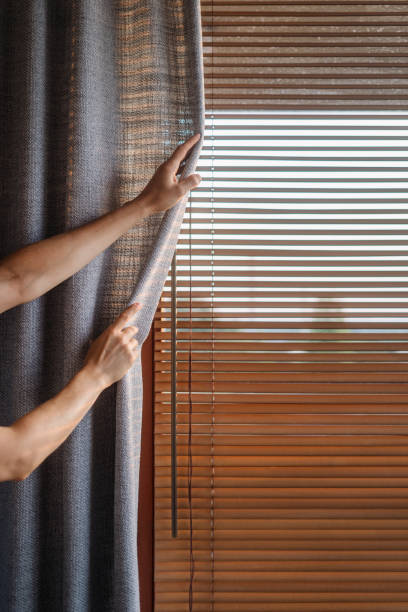 istock Morning light streaming through blinds as a person adjusts curtains indoors 2186251813