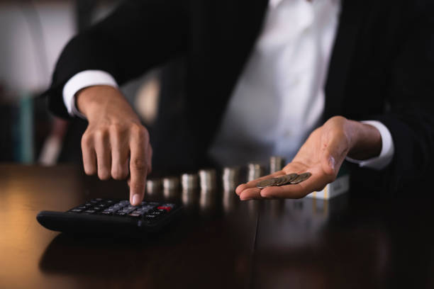 Businessman is calculating expenses and holding coins in his hand, demonstrating financial management and investment concepts