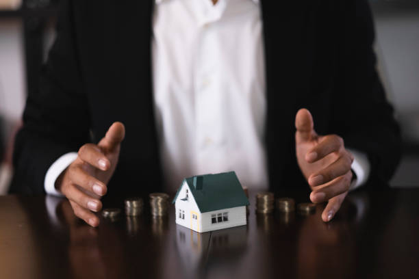 istock Real estate agent protecting a miniature house and coins on a table 2186260914
