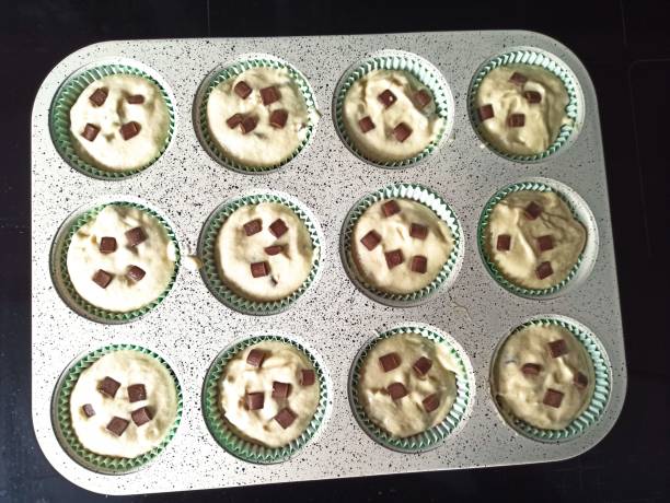 istock A muffin tray filled with batter and chocolate chunks sits on a kitchen counter, ready to be baked. The baking cups are lined and each has a generous amount of chocolate. 2186278356