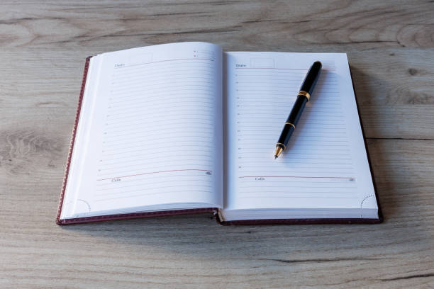 istock There is an open brown diary and a ballpoint pen on the table. A place for the text. 2186289568