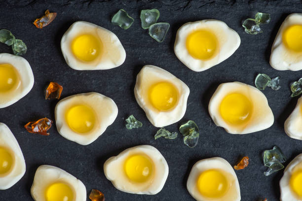 A selection of egg-shaped gummy candies with yellow centers arranged on a dark plate, accented by crystalline sugar pieces, creating a vibrant sweet display.