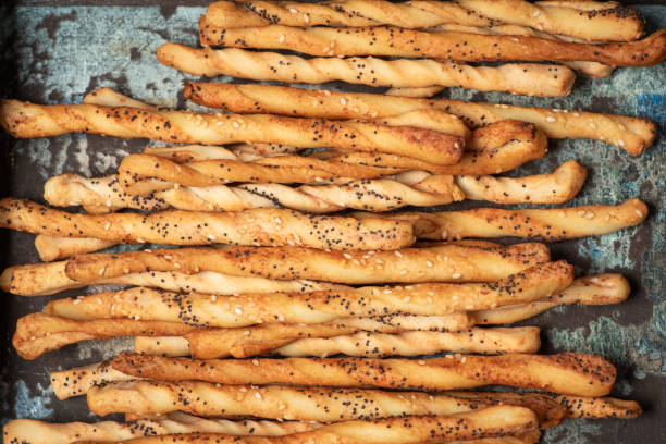 Delight in a collection of flavored and popcorn-studded breadsticks beautifully presented in a rustic wooden tray; the perfect savory treat for gatherings or solo indulgence.