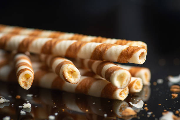 Five striped wafer sticks lying diagonally on a reflective surface, surrounded by scattered crumbs, showcasing a playful scene of delicacy and snack time enjoyment.