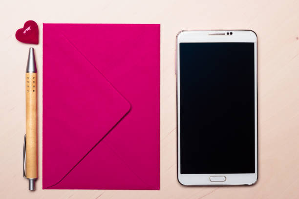 Pink envelope little heart, pen and smart phone on wooden surface.