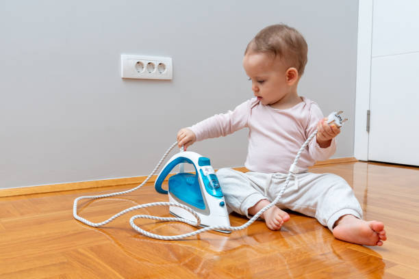A curious toddler exploring an iron cord, creating a potential safety hazard with an electrical outlet nearby