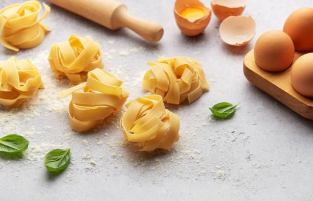 istock Fettuccine pasta nests with basil, eggs, flour and rolling pin on kitchen table 2186328841