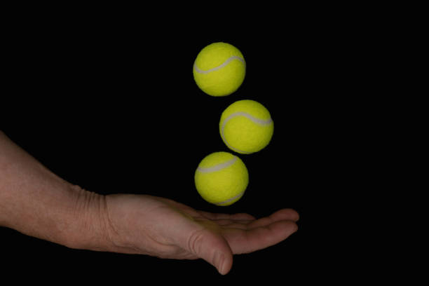 istock Hand balancing three bright yellow tennis balls on black background 2186334682