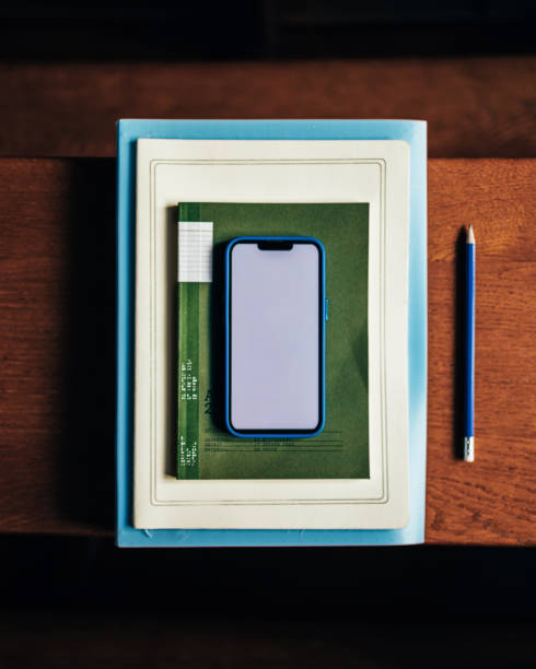An arrangement featuring a smartphone placed on stacked notebooks alongside a pencil on a wooden desk. Ideal for representations of technology, study, or work environments.