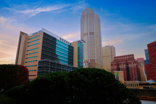 A striking architectural view of downtown Orlando, Florida, showcasing towering skyscrapers against a deep blue sky. The glass facade on the left reflects surrounding buildings, creating a dynamic contrast with the geometric patterns of the central high-rise.
