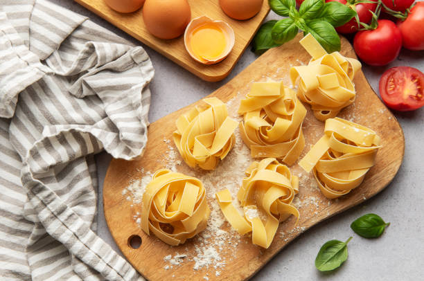 istock Uncooked tagliatelle pasta nests with basil, tomatoes and eggs on wooden cutting board 2186370231