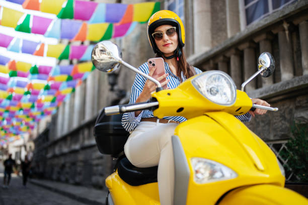 istock Woman sitting on yellow moped and using her phone. 2186379164