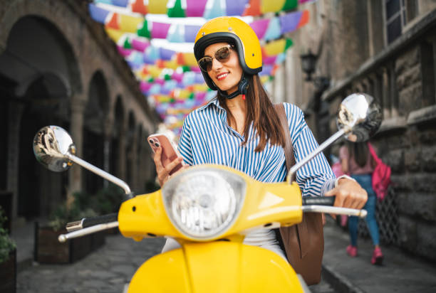 istock Woman sitting on yellow moped and using her phone. 2186379174