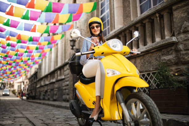 istock Woman sitting on yellow moped and using her phone. 2186379176