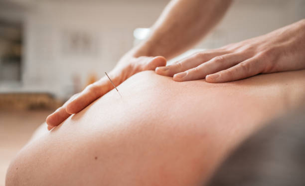 Half face of pretty smiling naked young indian woman enjoying lifting face massage in spa, white background, copy space. Wellness therapist hand rubbing chin of relaxed lady