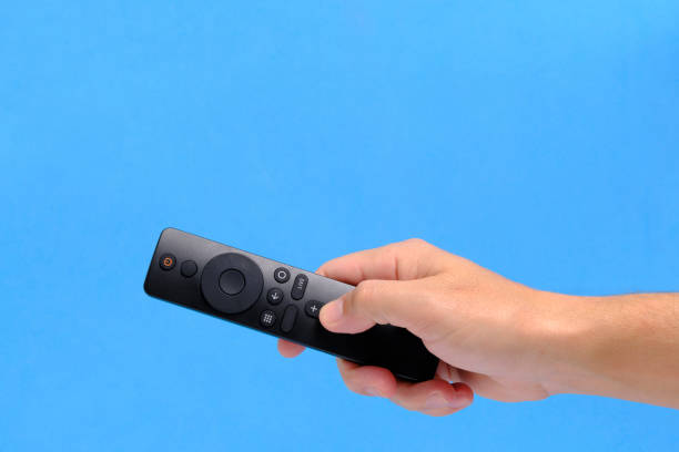 istock Hand blue background holds TV remote by pressing button with finger. 2186402955