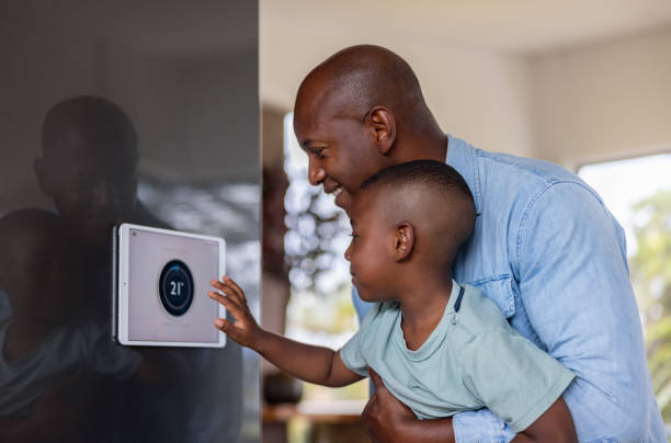 Father and son using a home automation system to lower the temperature African American father and son using a home automation system to lower the temperature of their house air conditioner family stock pictures, royalty-free photos & images