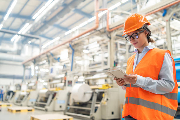 istock Female engineer using a tablet in a busy factory environment with machinery in background. 2186414129