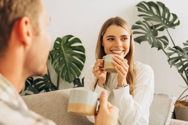 istock Happy, attractive woman drinking coffee, holding cup talking with man sitting on comfortable sofa 2186414266