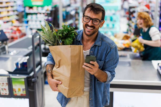 istock Smiling customer holding grocery bag and smartphone at checkout 2186420785