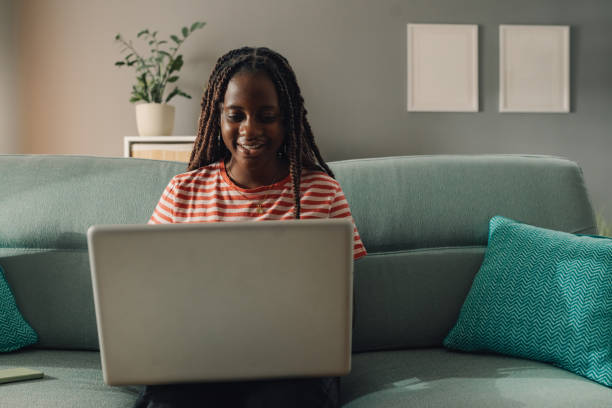 istock Young black woman working remotely from home office using laptop on sofa 2186421977