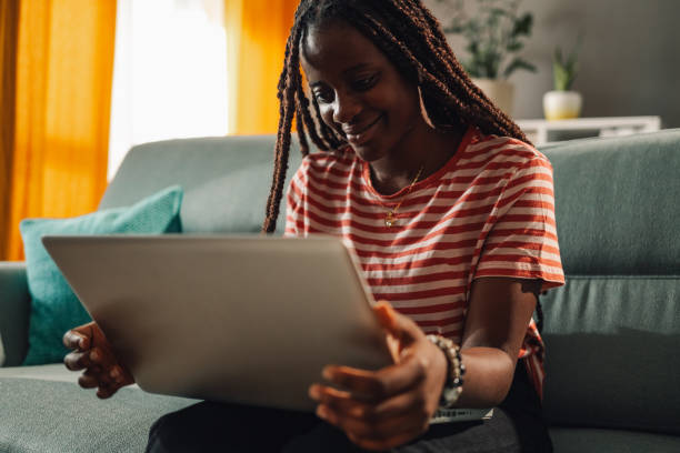 istock Young black woman working from home sitting on the couch using laptop computer 2186421997