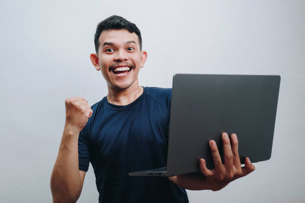 istock an asian young man showing happy expression while holding his laptop, isolated on white. finance ads concepts. 2186426727