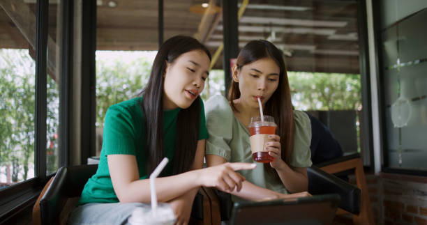 istock Two young women are watching something together on a tablet and drink a cold drink 2186427043