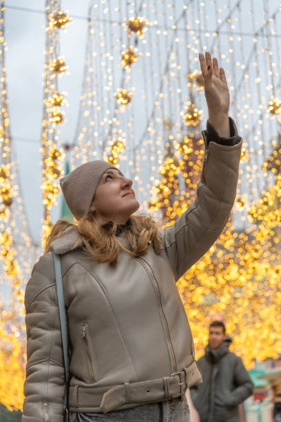 istock Woman stands with raised arm under light garland 2186444591