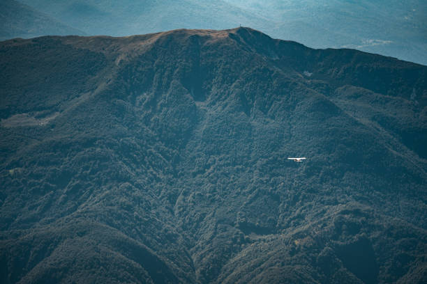 A small aircraft is captured mid-flight against the vast greenery of mountainous terrain, emphasizing the scale and solitude of panoramic aviation experiences.
