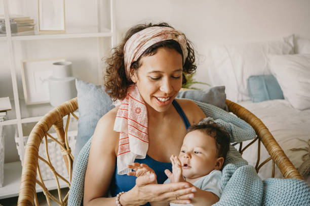 Portrait of attractive happy young mixed race mother holding her newborn baby boy, lulling him to sleep while sitting in basket chair and smiling. Motherhood, childcare, nursery and parenting concept retrato de una atractiva madre joven feliz de raza mixta que sostiene a su bebé recién nacido, arrullándolo para que se duerma mientras está sentada en una silla de cesta y sonriendo. concepto de maternidad, cuidado de niños, guardería y crianza