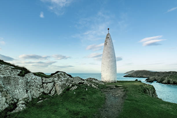 istock A white lighthouse stands out on the rocky coastline, surrounded by grass and cliffs. The calm ocean stretches out under a clear blue sky, creating a sense of tranquillity. 2186457602