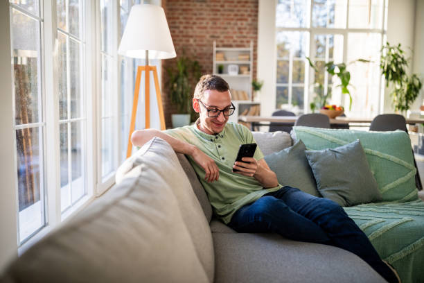 istock Man relaxing on couch with smartphone in hand 2186458148